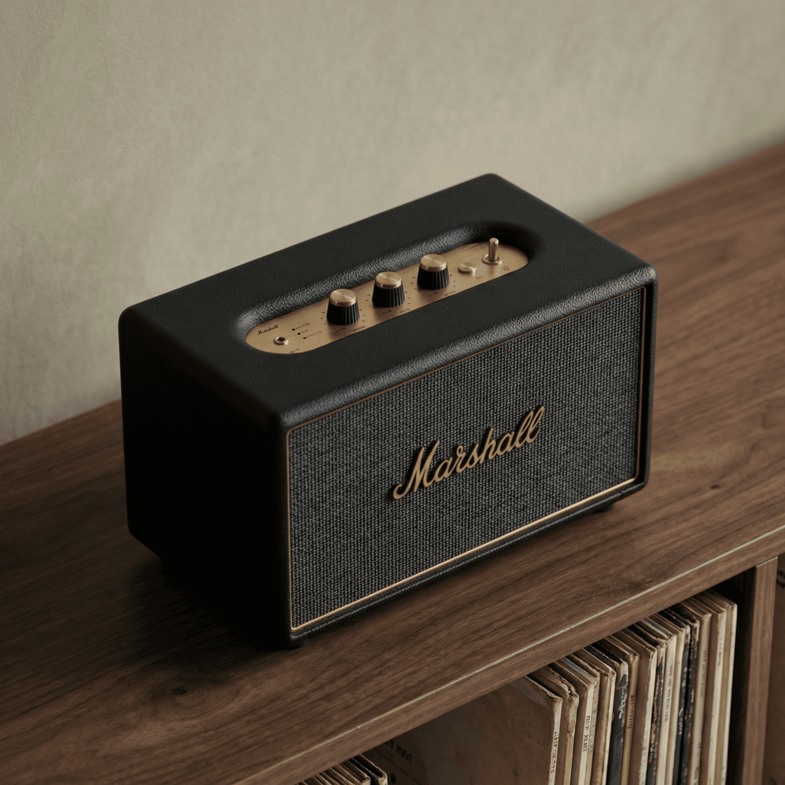 Marshall Bluetooth speaker with gold controls on a wooden shelf near vinyl records