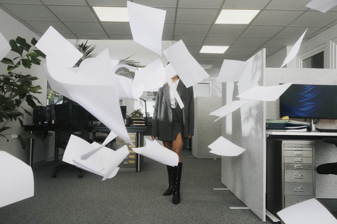 Woman in office surrounded by flying papers, symbolizing marketing metric chaos