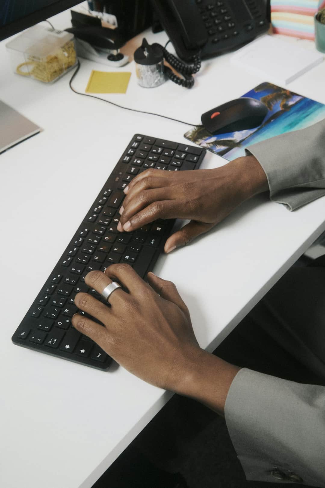Hands typing on black keyboard at office desk during spreadsheet work