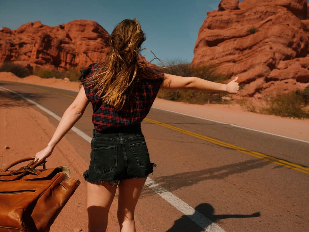 Woman wearing plaid shirt on desert road with red rock formations in background