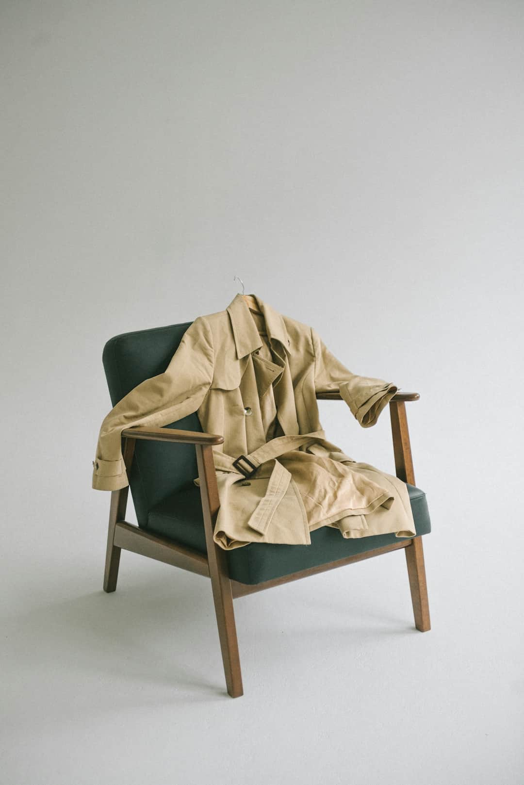 Modern accent chair with green upholstery, wooden legs, and cream fabric drape