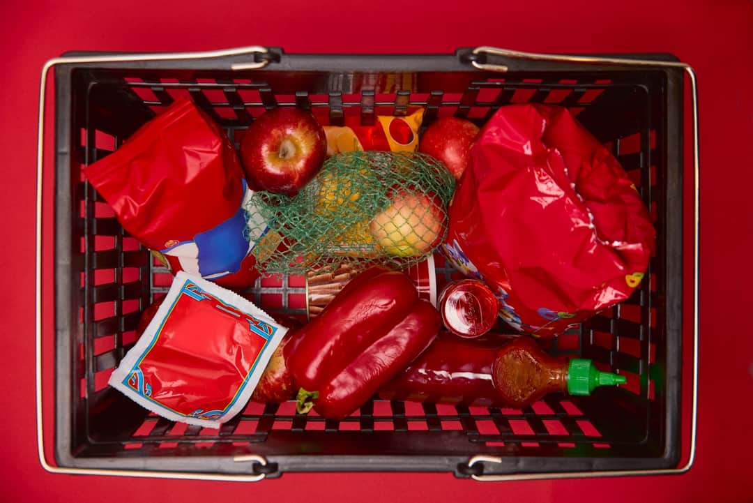Red plastic shopping basket with fresh bargain peppers, tomatoes and onion
