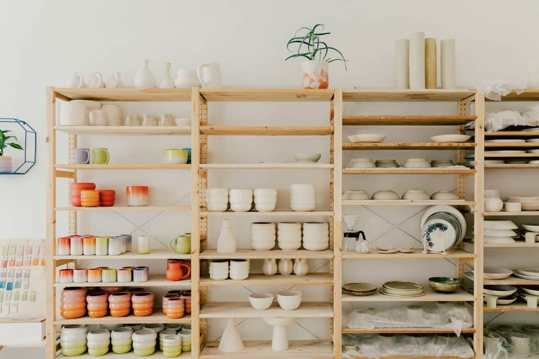 White and colored porcelain bowls and vessels displayed on wooden shelves in a showroom