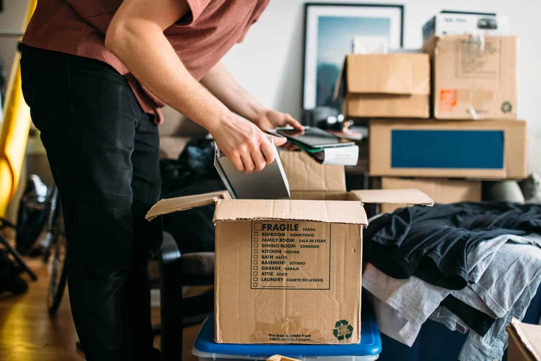 Person packing fragile box during office migration with cardboard boxes stacked in background
