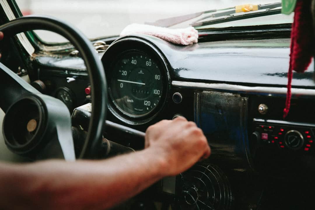 Hand on steering wheel inside vintage Cuban car with visible speedometer