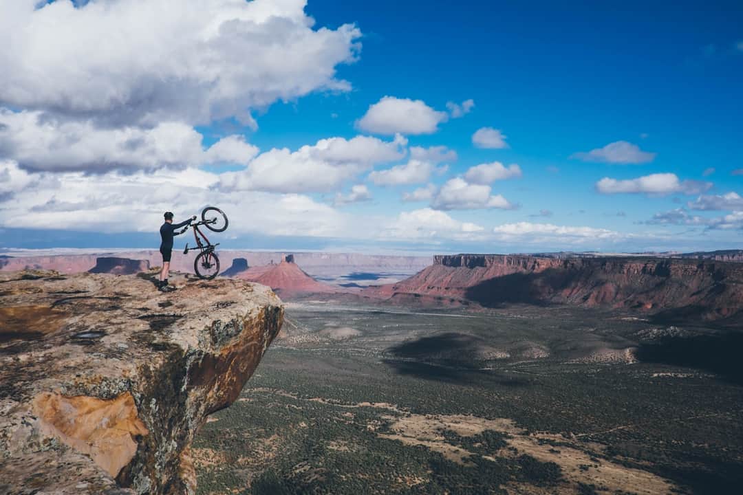 Mountain biker on rocky cliff overlooking Moab desert landscape