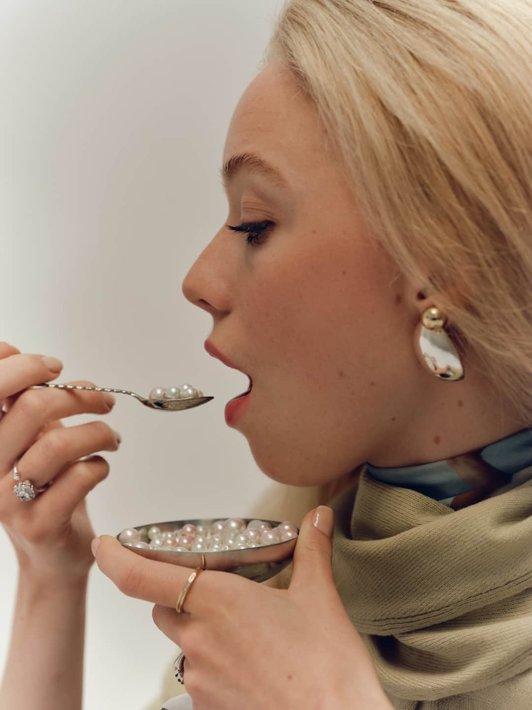 Woman wearing pearl drop earrings and rings eating caviar, luxury portrait