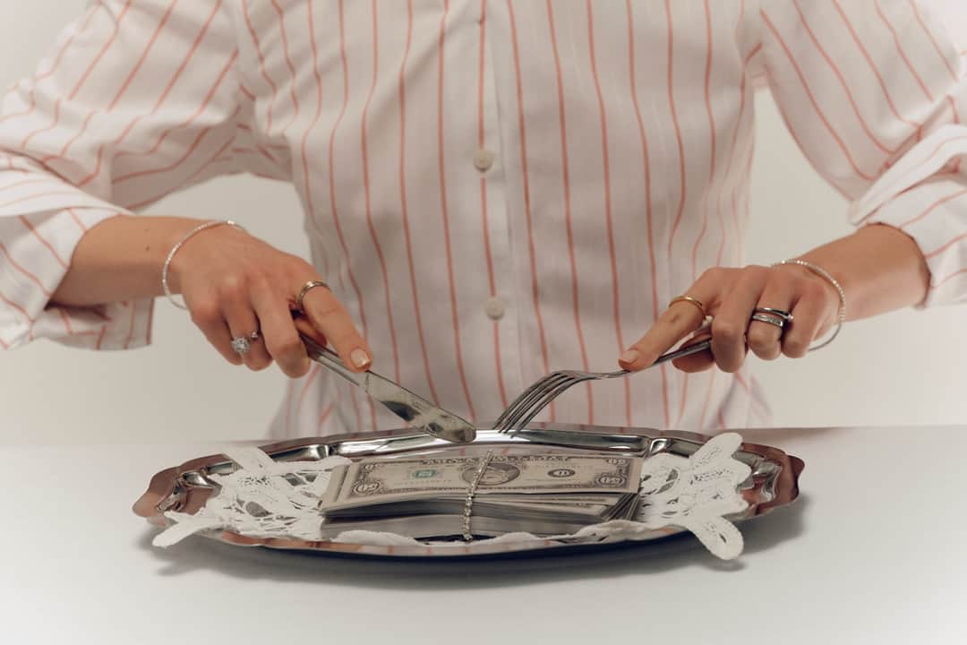 Woman with fork and knife cutting stacked dollar bills on plate, E-A-T metaphor