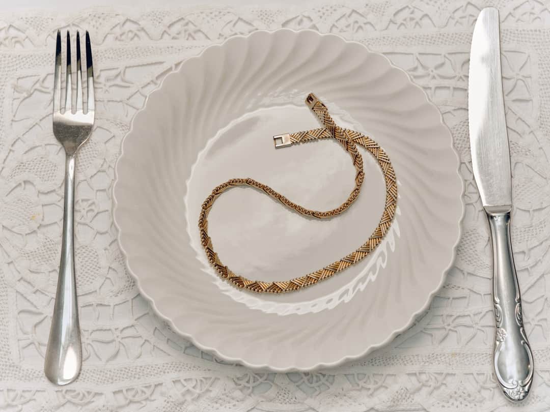 Gold rope chain jewelry on white plate with formal place setting