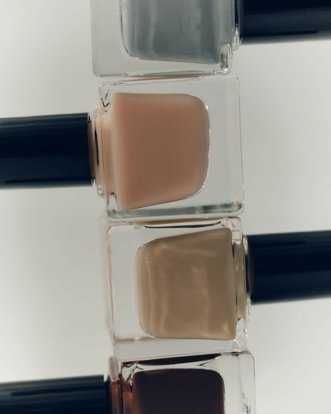 Three nail polish bottles in gray, nude, and tan shades with black caps