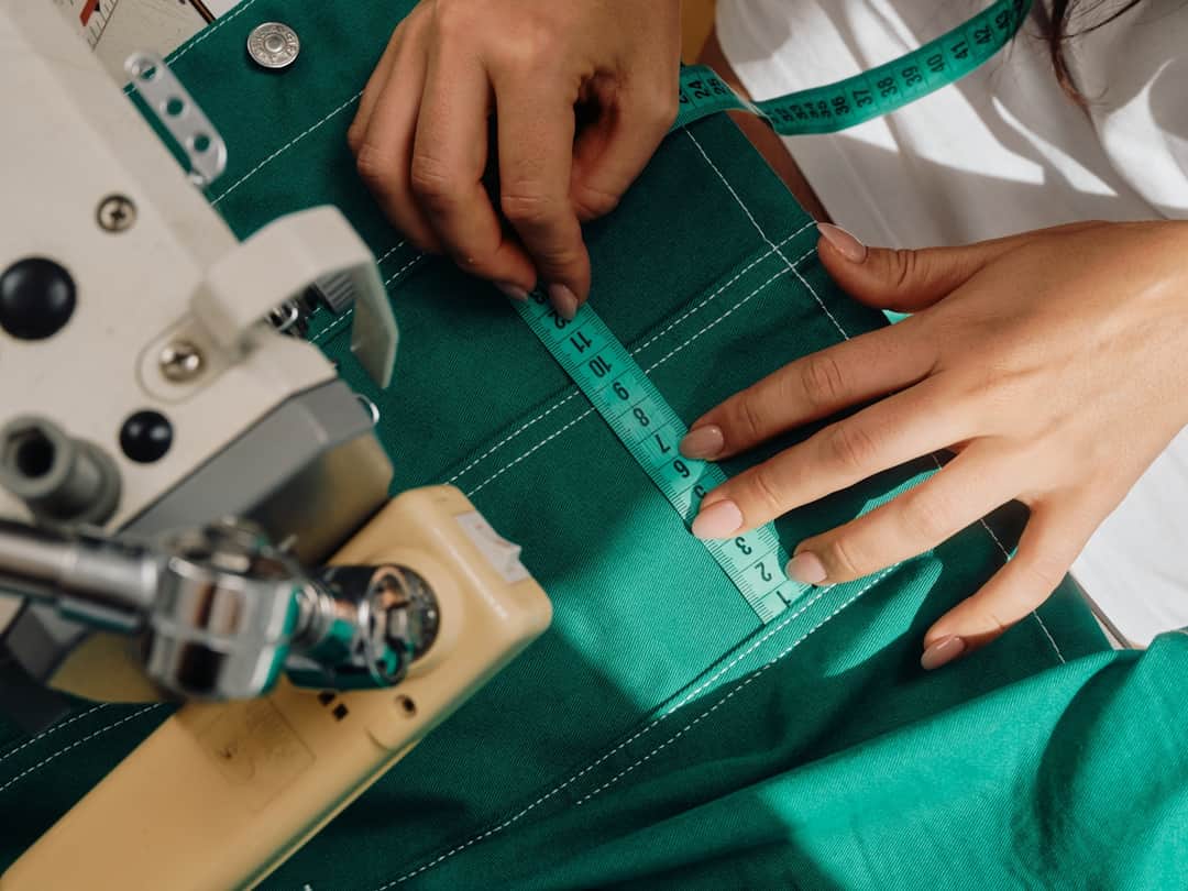 Hands measuring green fabric with precision tools in professional studio workspace