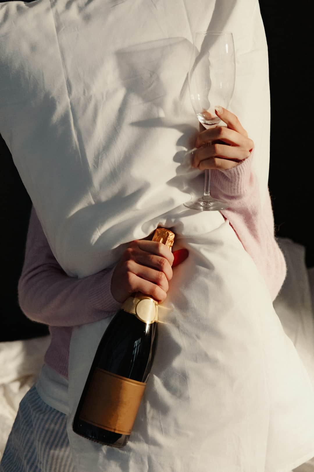 Hand holding champagne bottle in sunlight casting shadows on white fabric
