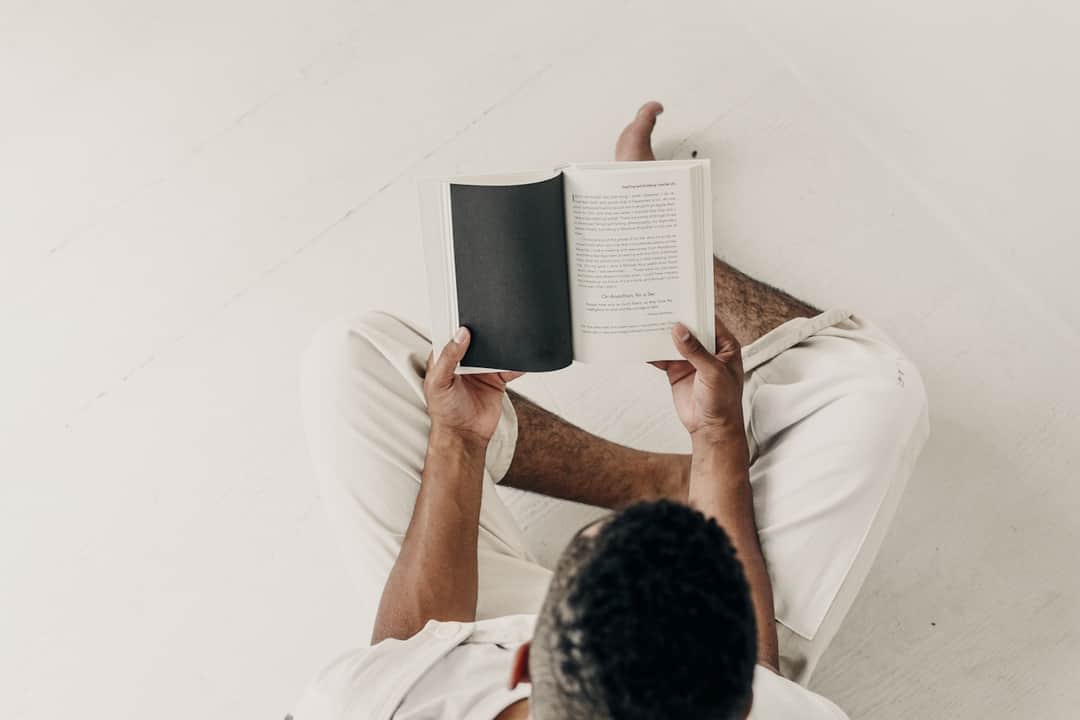 Man reading book on white bed, engaged with quality content