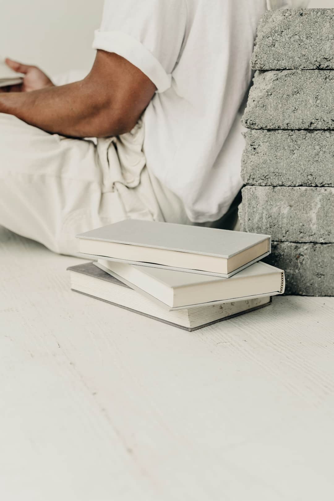Person leaning against concrete wall with stacked white books representing algorithm research