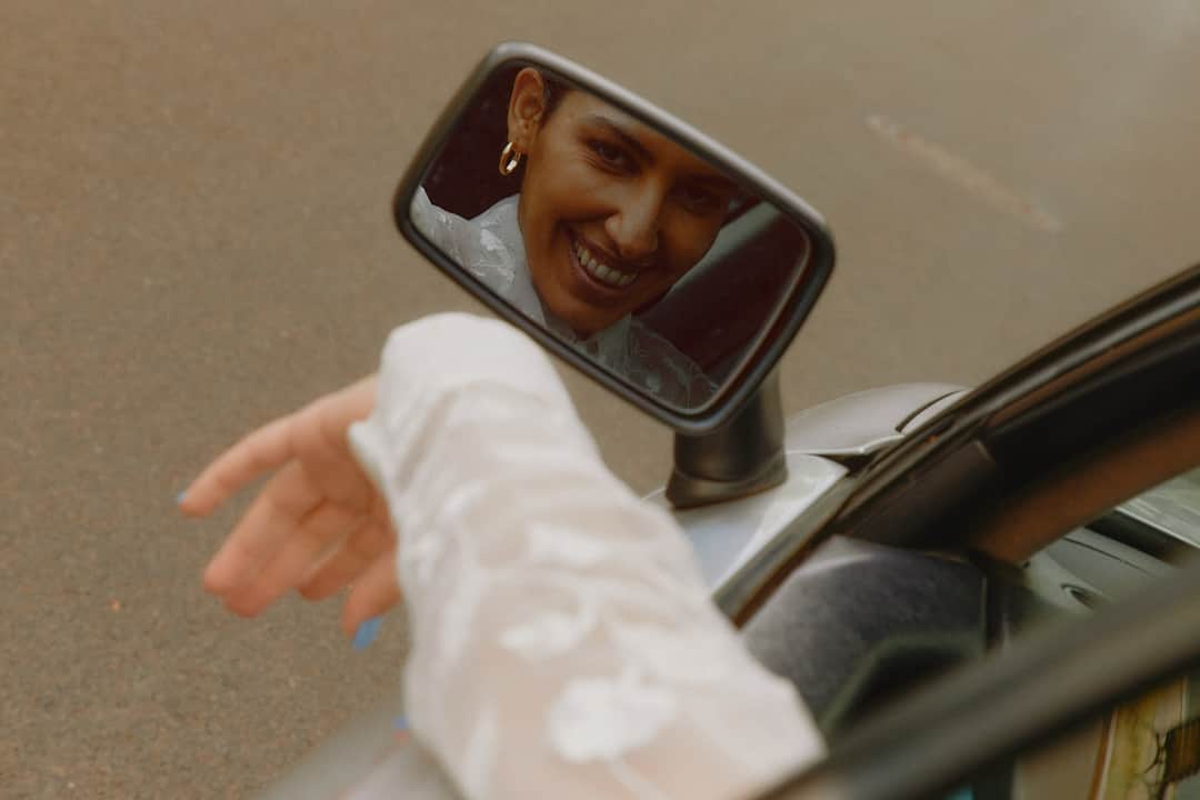 Woman smiling in car mirror waving, embodying stress-free car rental experience