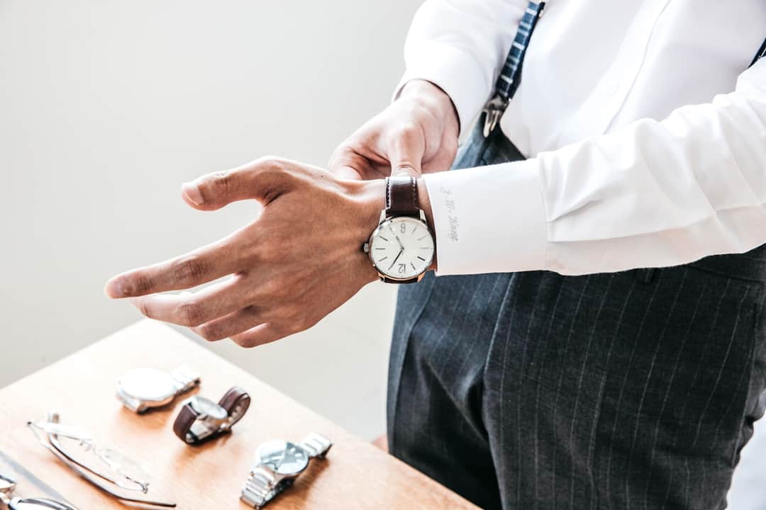 Man displaying minimalist watch with black leather band and other luxury timepieces on table