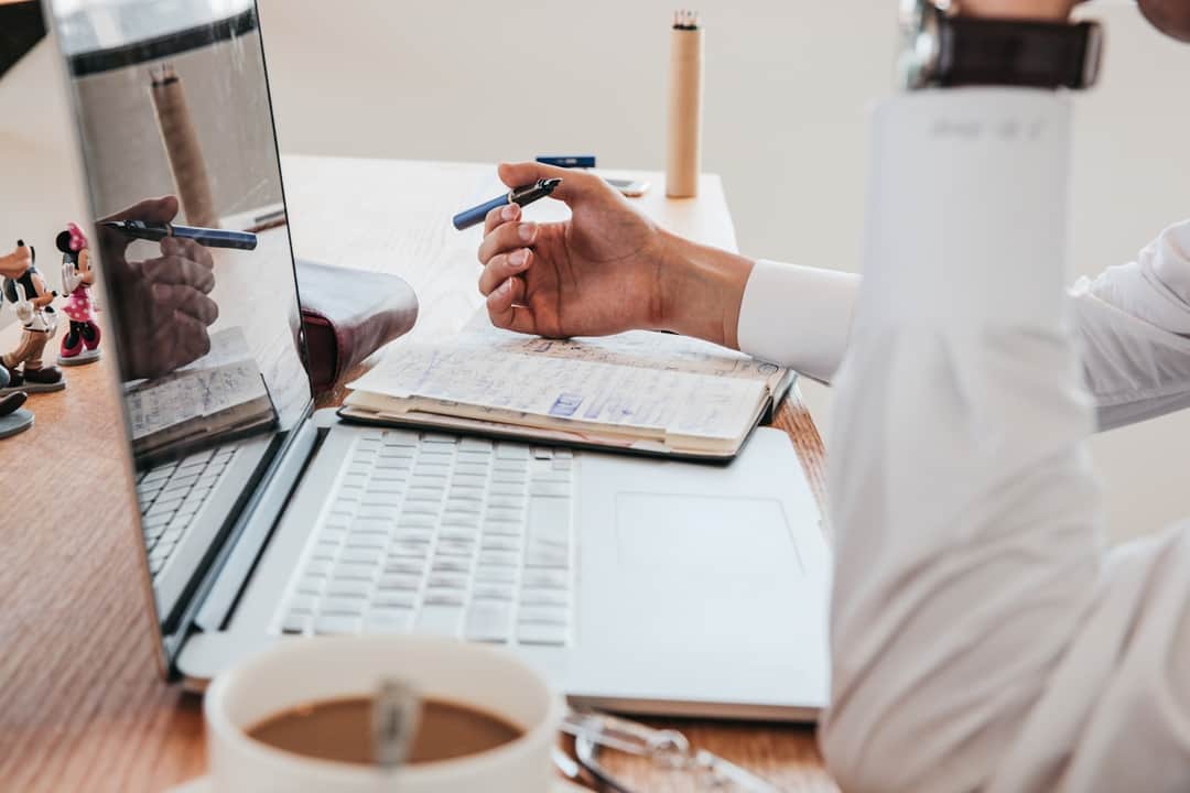 Content marketer writing notes at desk with pen, notebook, and laptop
