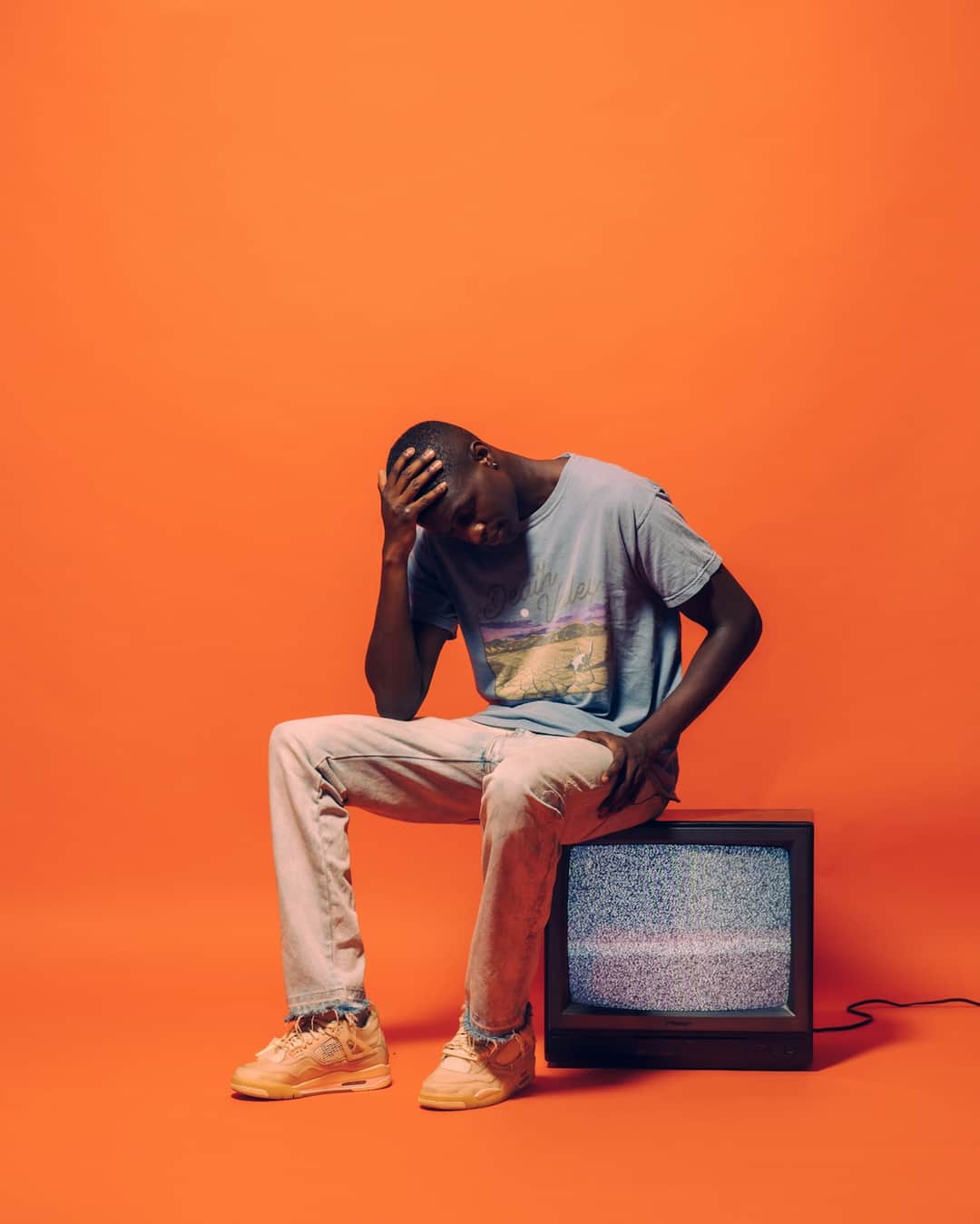 Person holding head in frustration sitting on television with static on orange background