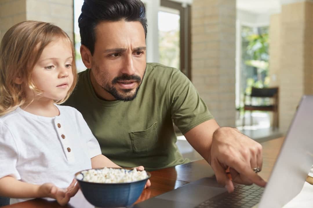Father and child viewing content on laptop together at home