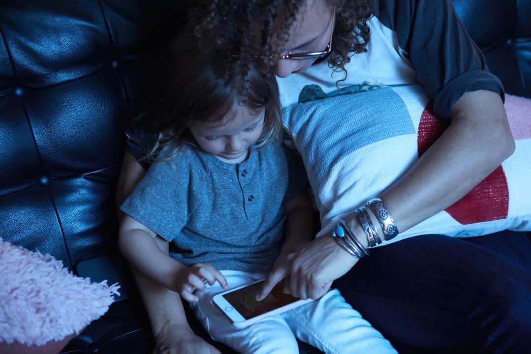 Parent and child engaged with digital device on modern home sofa