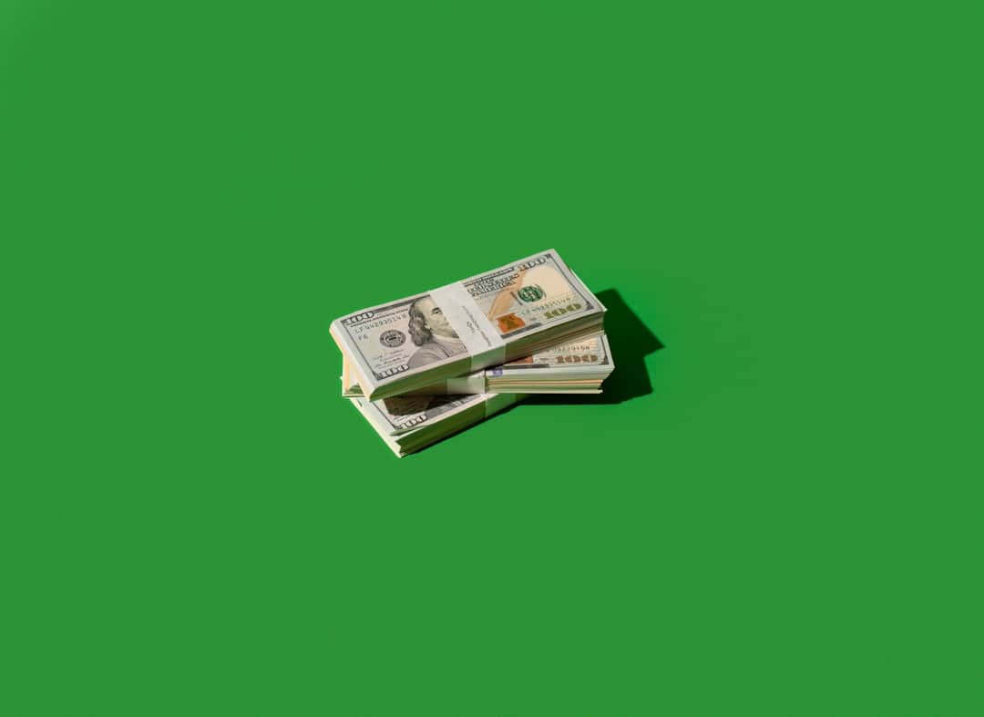 Stacks of $100 bills on green background illustrating grant funding for charities