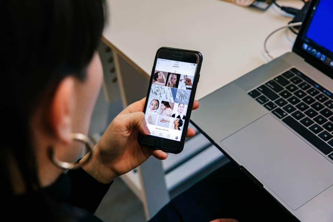 Person holding smartphone showing social media feed at workplace desk