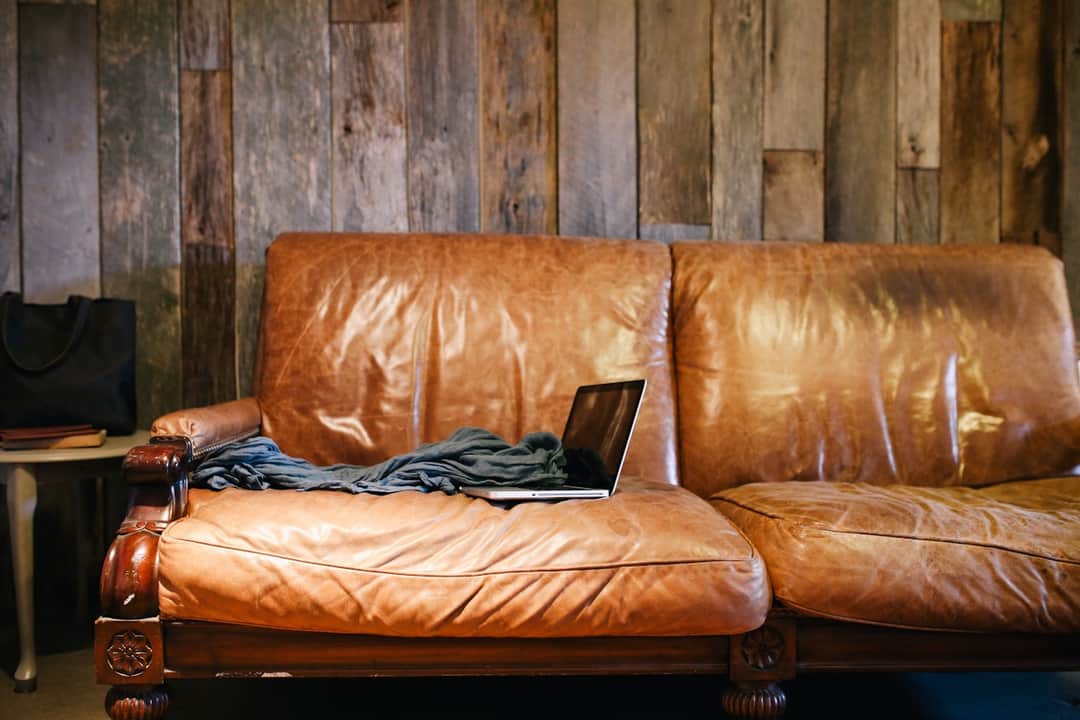 Brown leather sofa with layered cushions against wooden wall