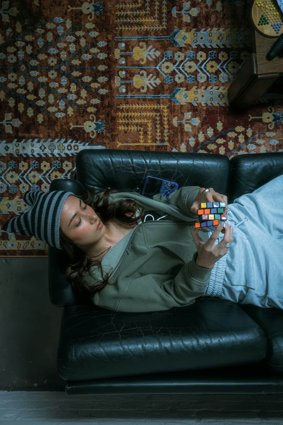 Woman lounging on black leather sofa solving Rubik's cube from above