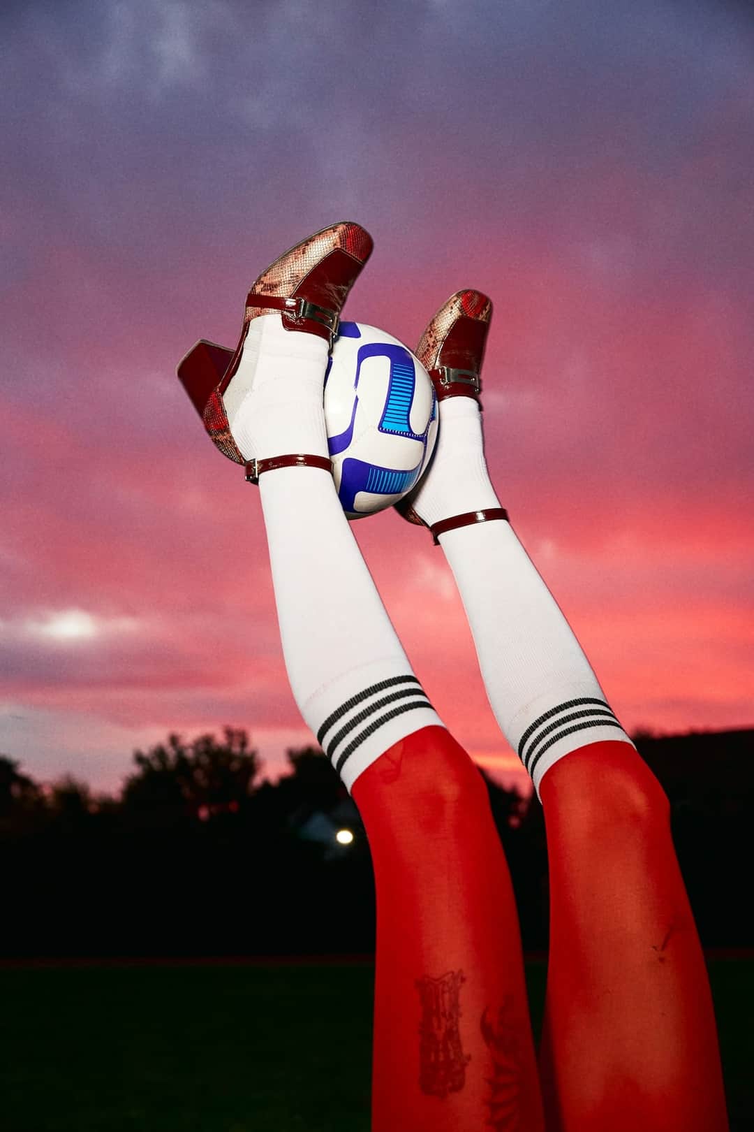 Red D2C soccer cleats with blue accents and white socks against sunset sky