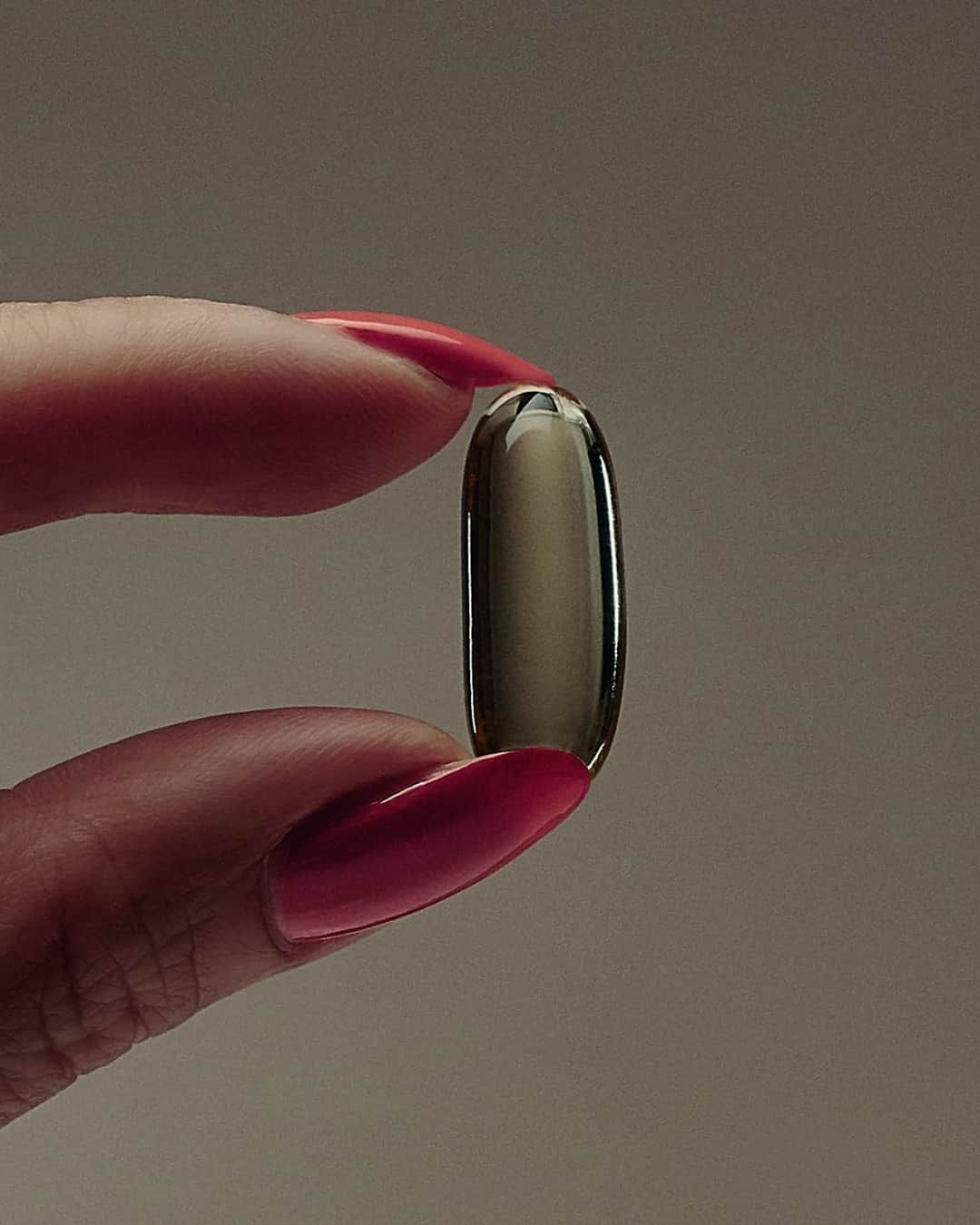 Woman holding supplement capsule with hot pink manicure