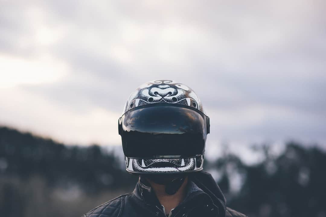 Rider wearing black skull and crossbones motorcycle helmet against blurred landscape background