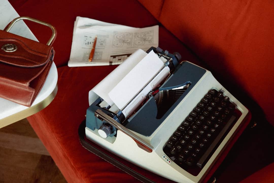 Vintage typewriter and creative workspace on red fabric with design sketches, pencil, and leather accessories