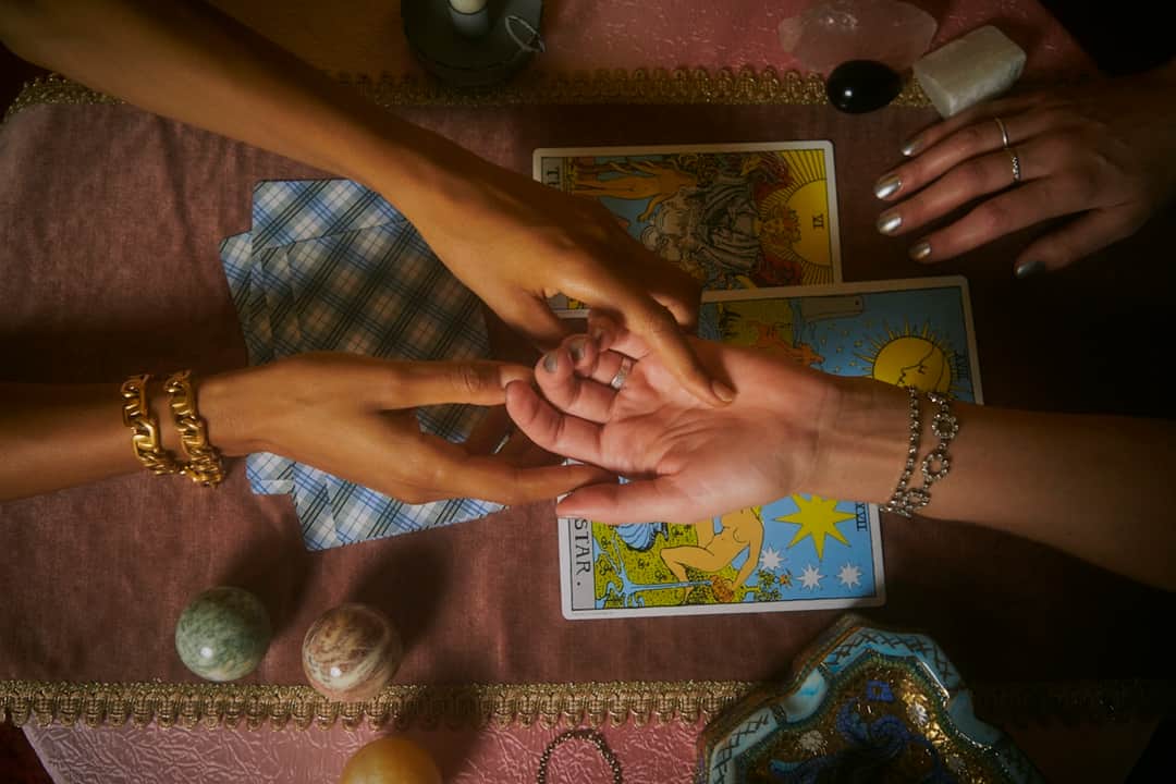 Hands performing tarot reading with amethyst crystals and gold bracelets