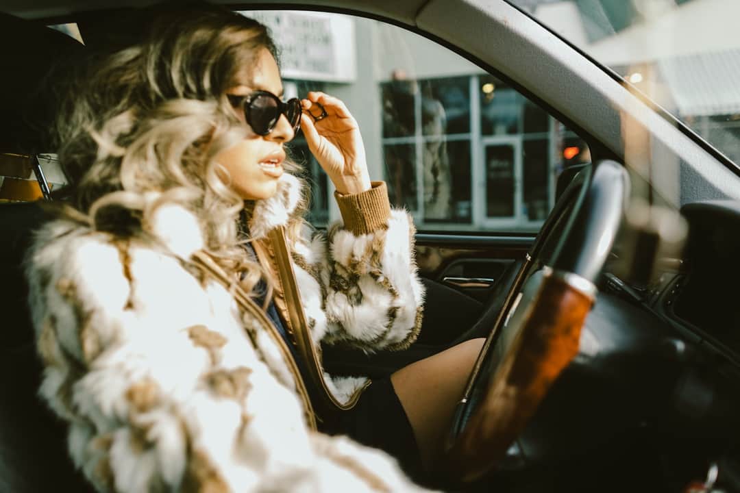 Woman in patterned jacket adjusting sunglasses in rental car on staycation