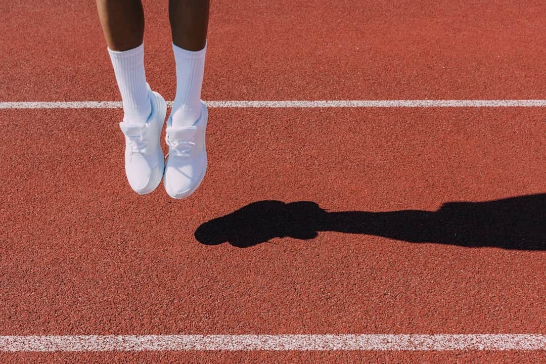 White athletic trainers on running track with athlete's shadow, highlighting footwear visibility