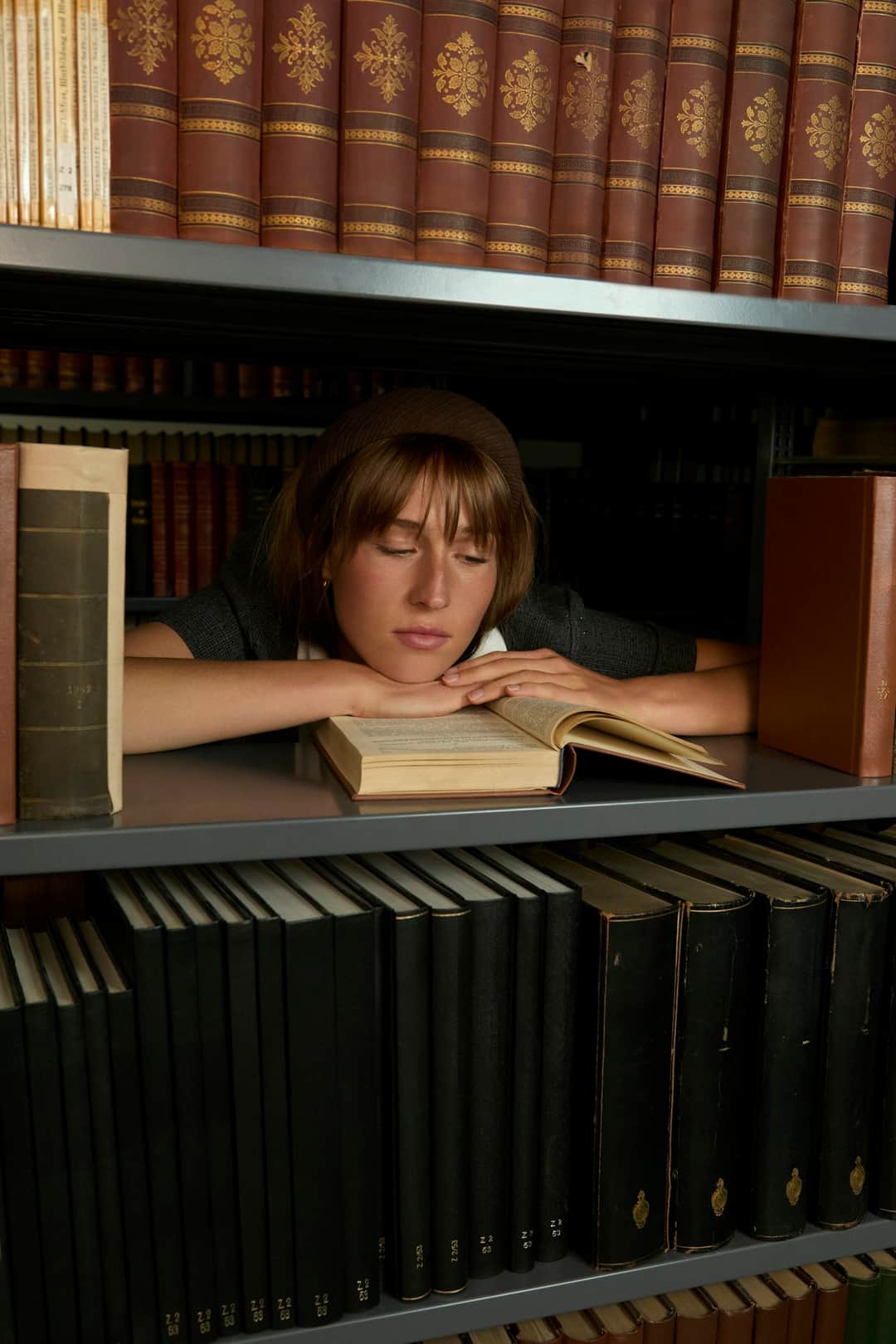 Woman reading from book on shelf surrounded by reference materials