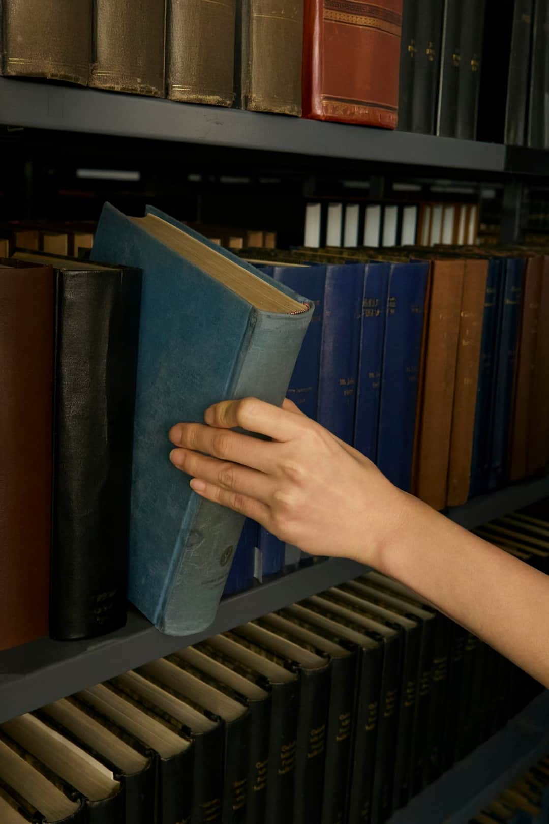 Hand selecting a blue hardcover book from a wooden library shelf