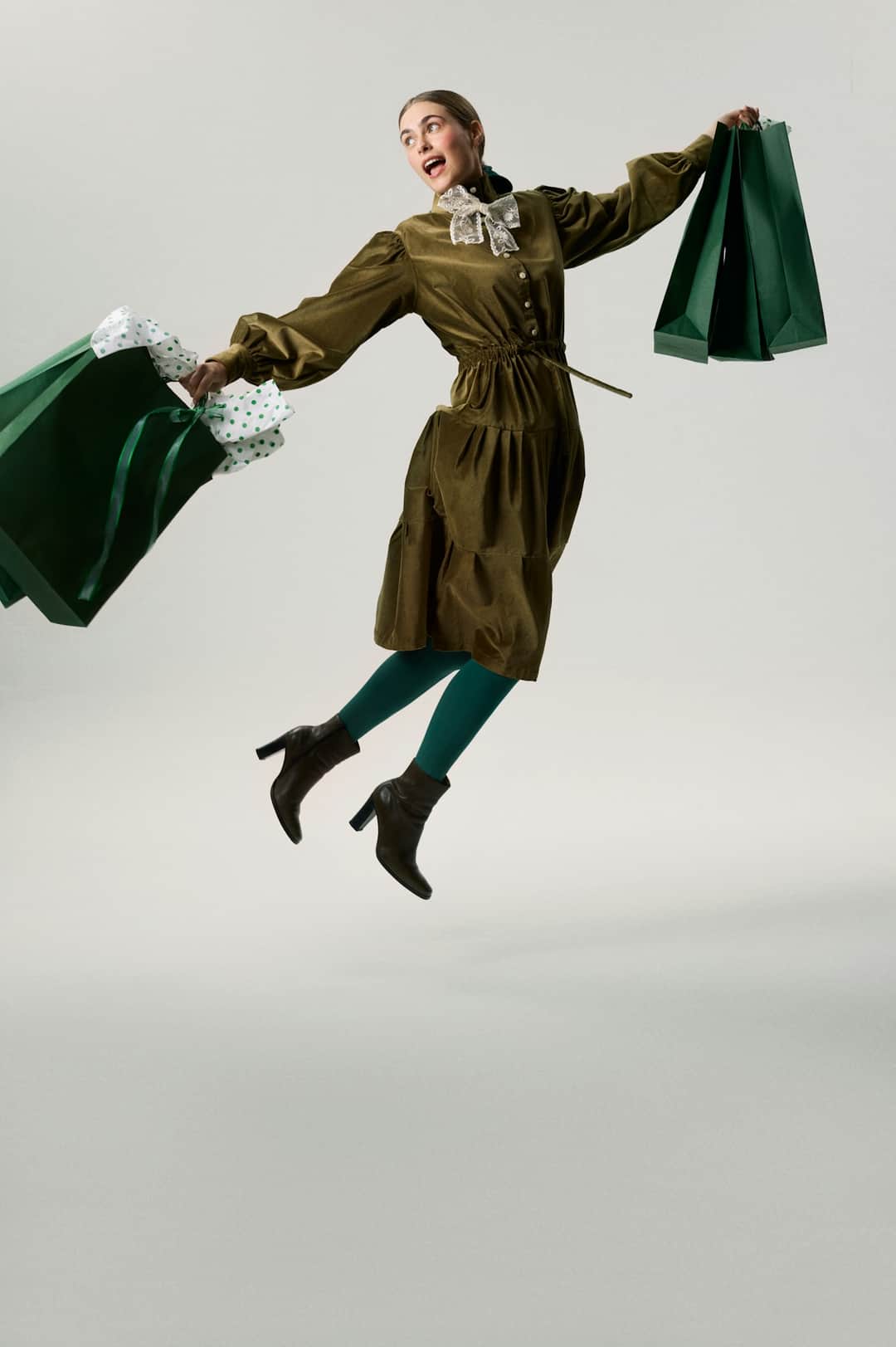 Excited shopper jumping with multiple full green shopping bags