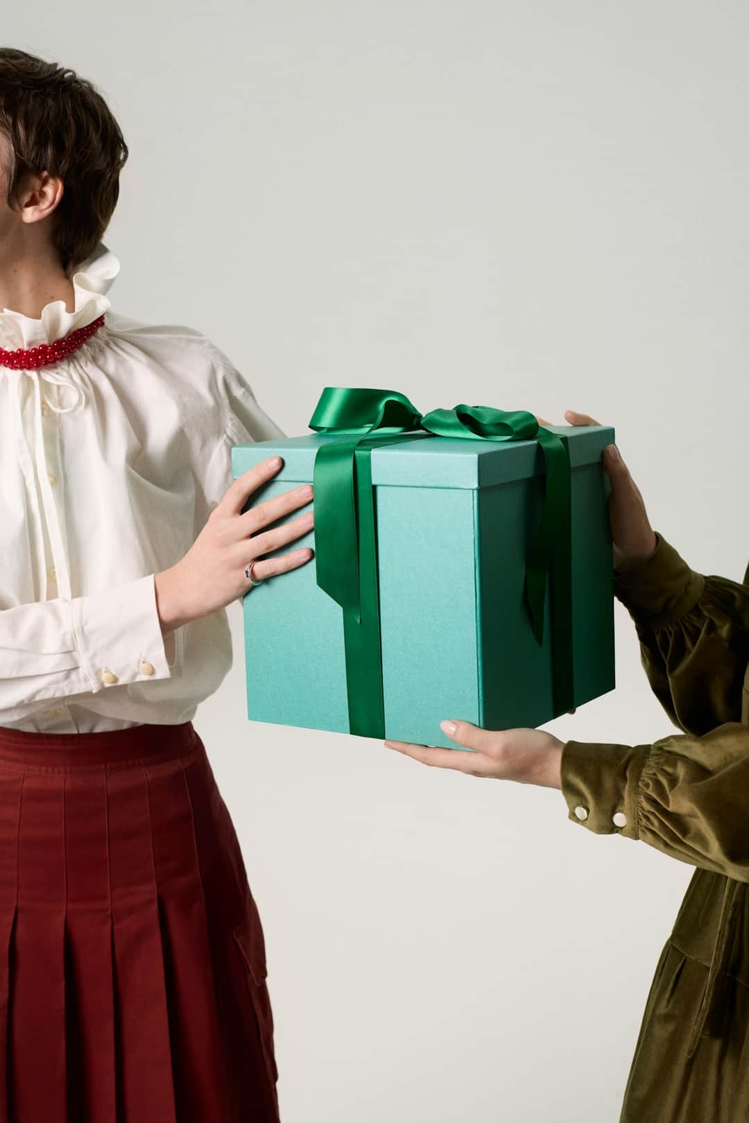 Woman in white shirt giving turquoise wrapped gift with green ribbon