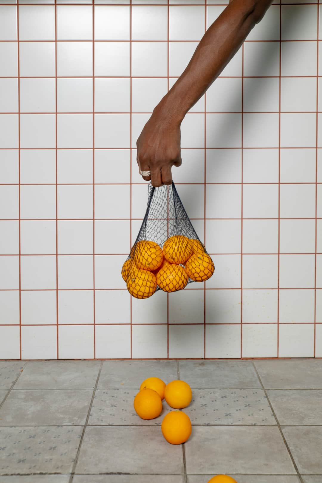 Hand dropping mesh bag of oranges with some falling to ground, representing hidden costs
