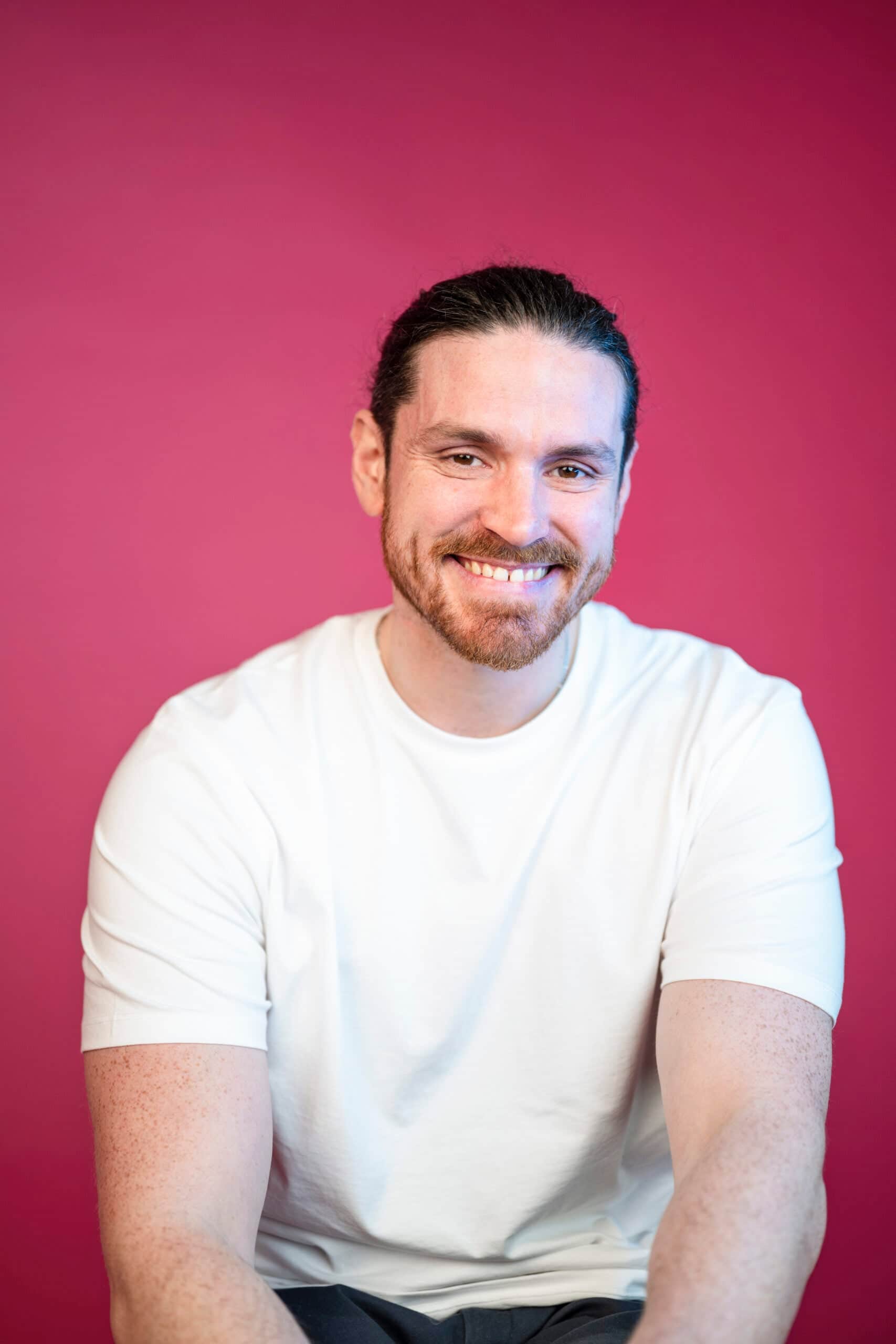 Smiling man with beard in white t-shirt against vibrant pink studio background