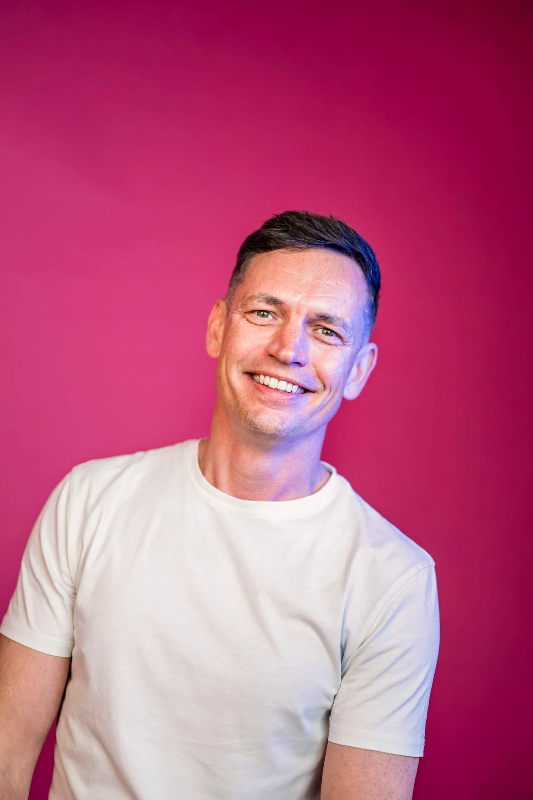 Marketing professional smiling at camera in white t-shirt on pink backdrop