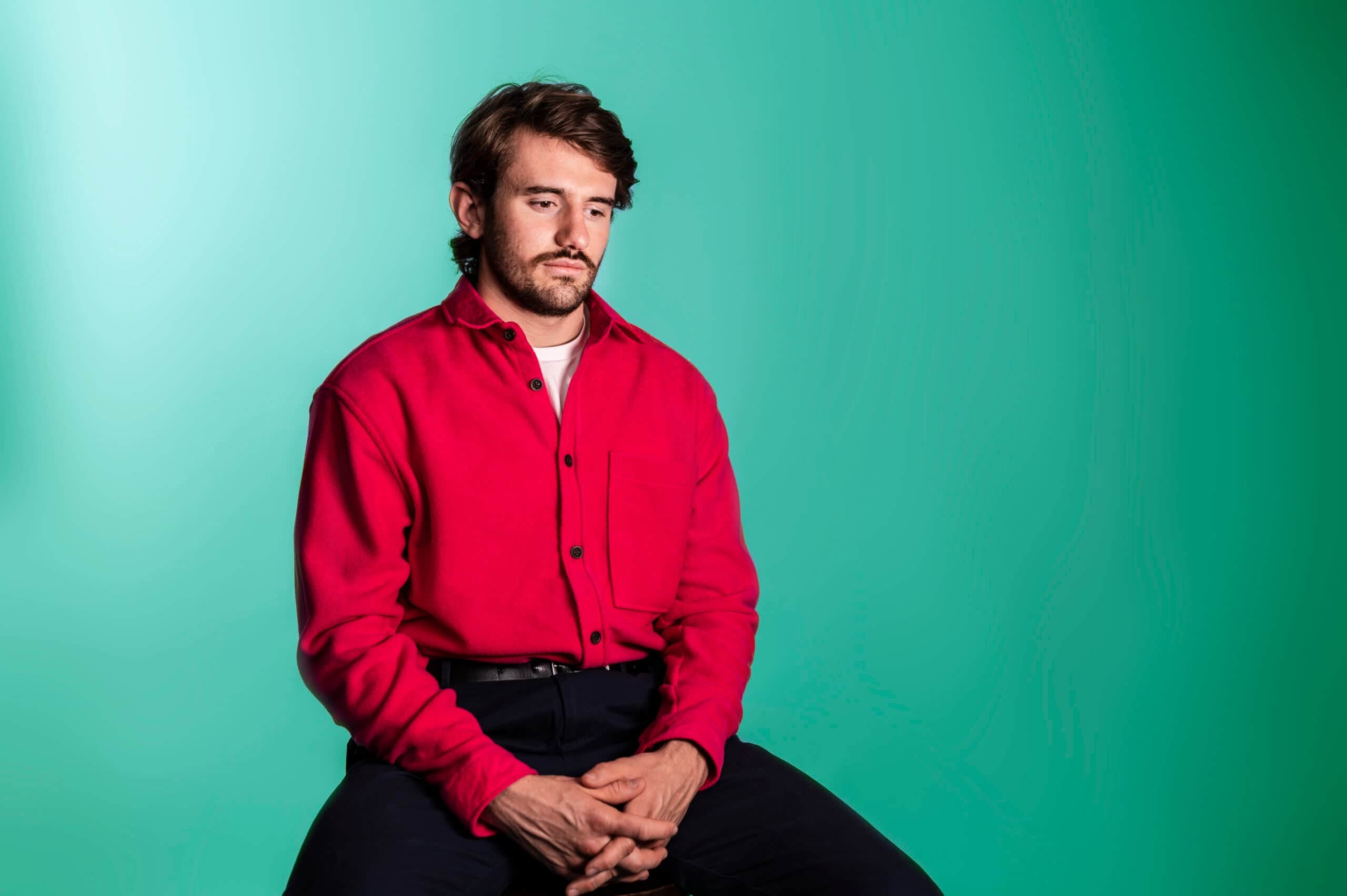 Man in red shirt sitting against turquoise background, representing team member at Salience marketing agency.