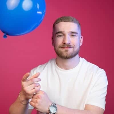 Owen from Salience search marketing agency pointing at camera against pink background with blue balloon