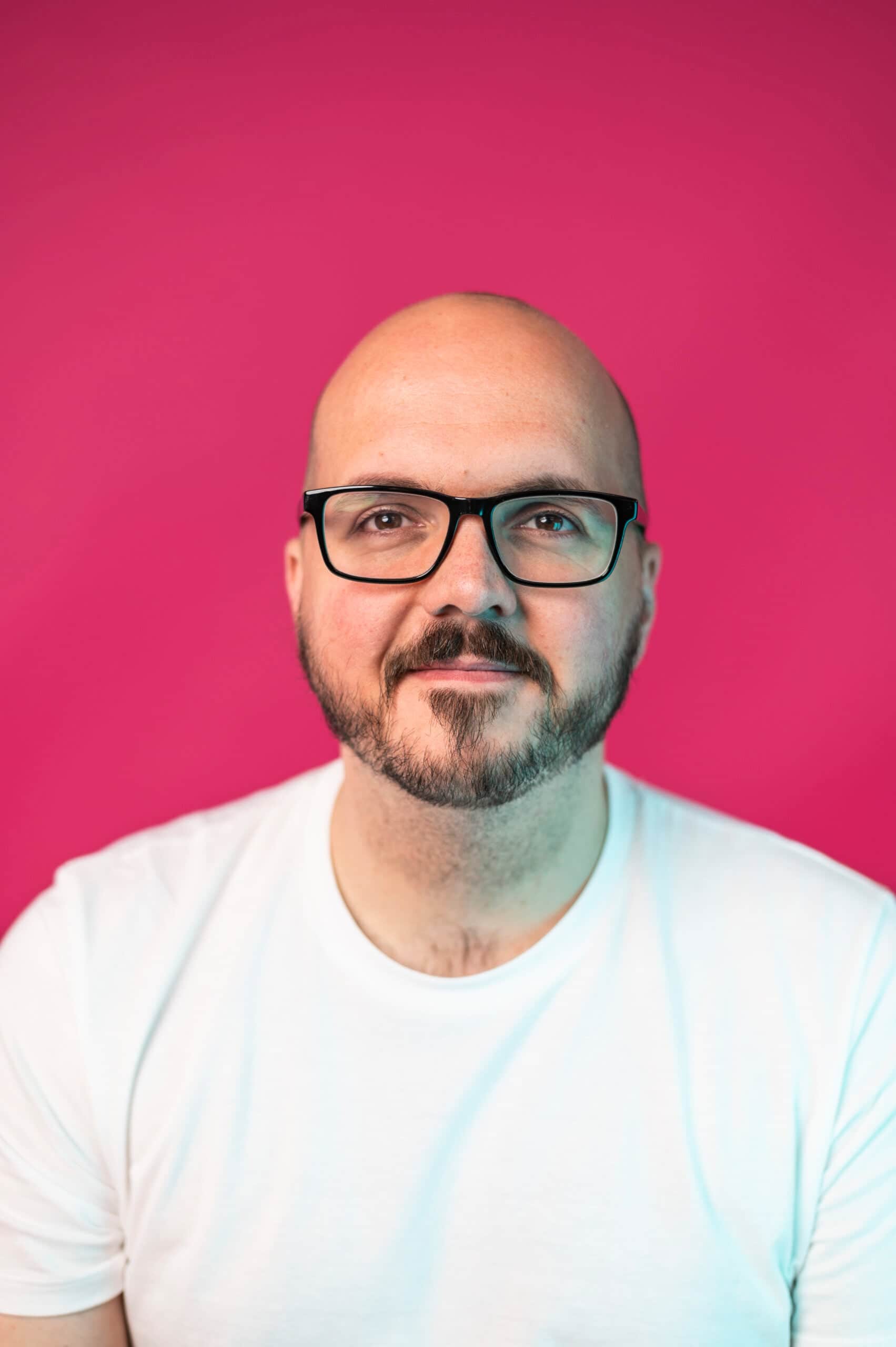 Male professional with glasses wearing white shirt against pink studio background