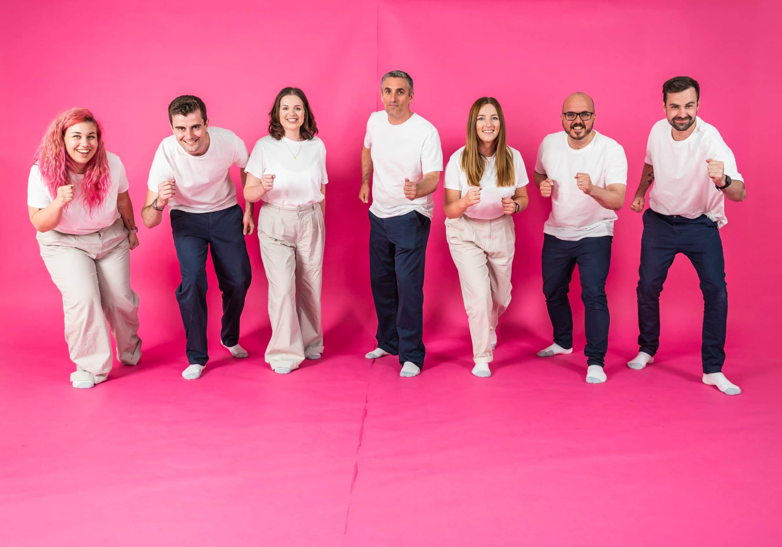 Salience team members in casual clothing posing energetically against a pink background.