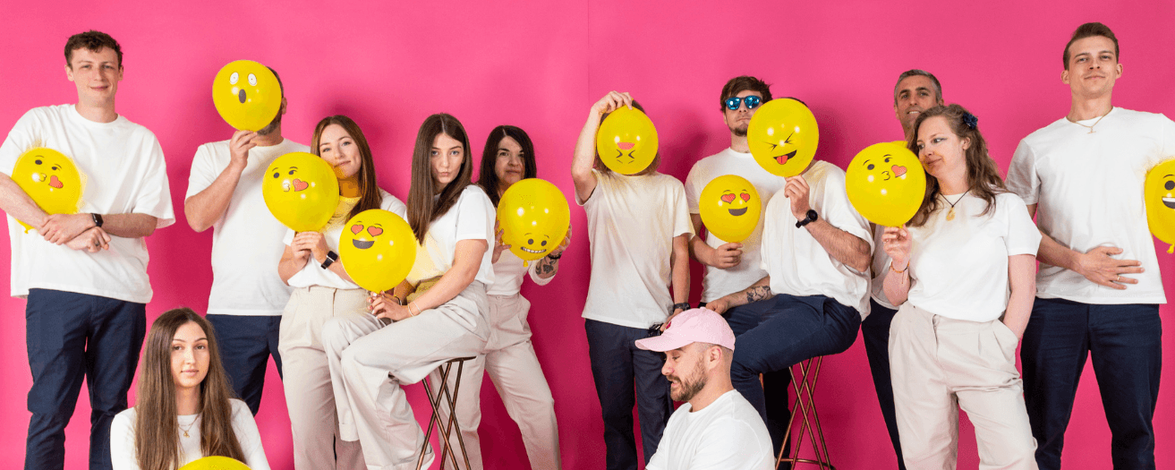 Team holding emoji balloons against pink background, representing creativity at Salience marketing agency.