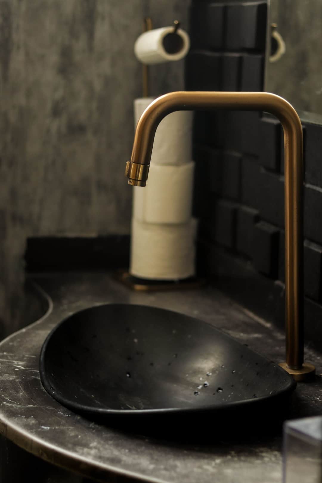 A modern bathroom sink with a sleek black basin and brass faucet, complemented by a stylish interior design. (Photo: Guilherme Simão via Pexels)