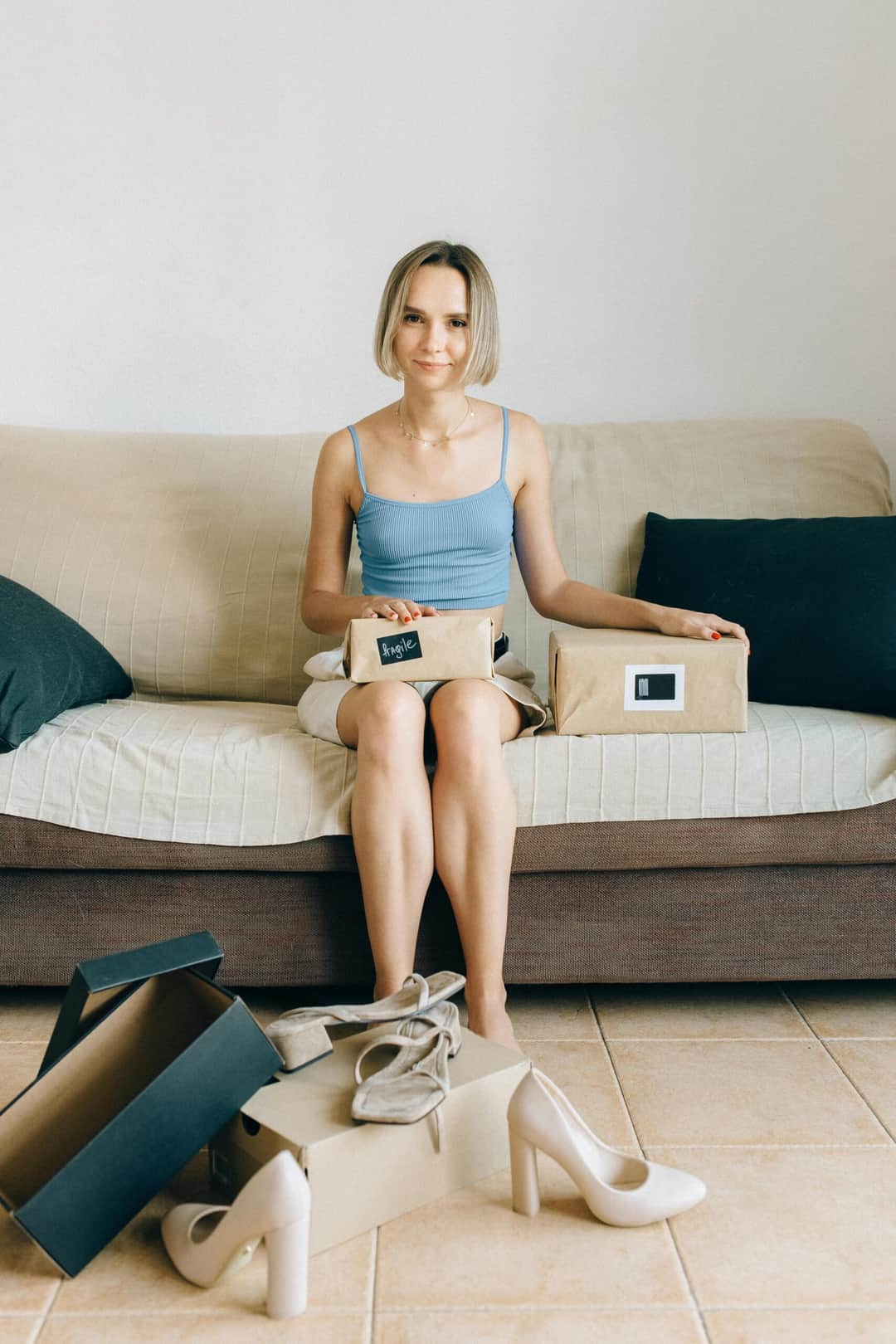 A woman comfortably seated on a sofa unpacks new shoes, enjoying a relaxed day at home. (Photo: Nataliya Vaitkevich via Pexels)