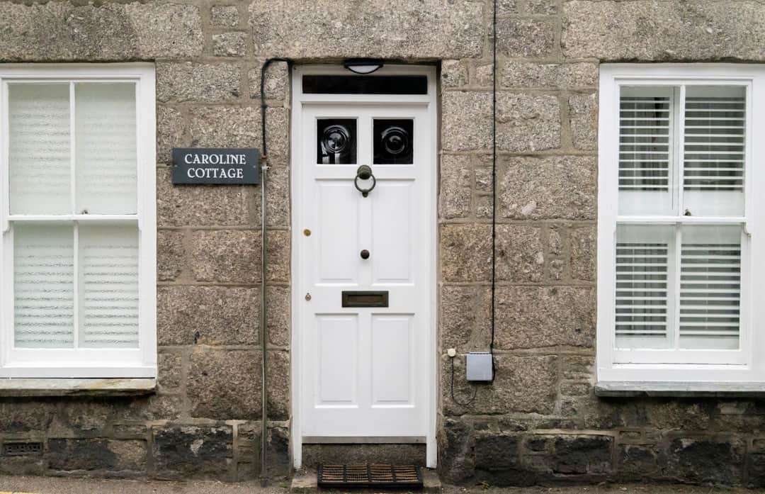 Elegant traditional entrance of Caroline Cottage in Penzance, Cornwall, featuring a symmetrical white door and stone facade. (Photo: Julia Barrantes via Pexels)